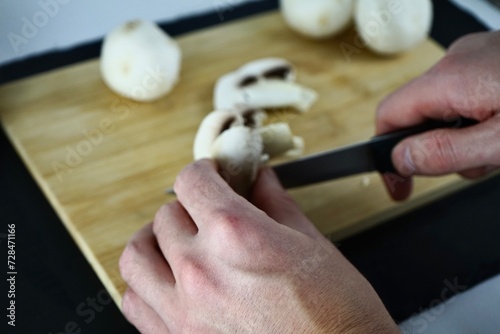 Male hands cutting champignons on a wooden board