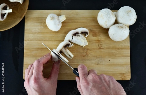 Male hands cutting champignons on a wooden board