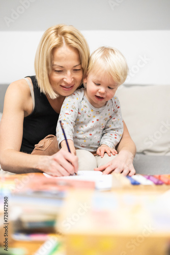 Caring young Caucasian mother and small son drawing painting in notebook at home together. Loving mom or nanny having fun learning and playing with her little 1 5 year old infant baby boy child
