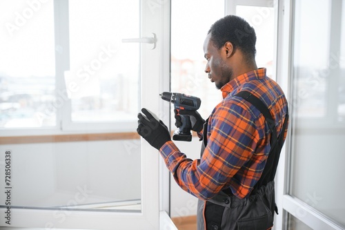 Workman in overalls installing or adjusting plastic windows in the living room at home