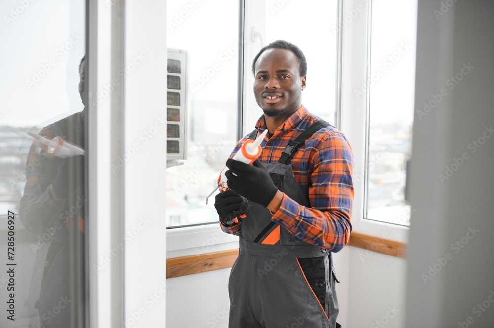 Workman in overalls installing or adjusting plastic windows in the living room at home Workman in overalls installing or adjusting plastic windows in the living room at home
