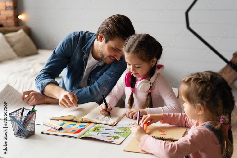 Caring young father helping little daughter with homework. Attentive small schoolgirl studying at home with young daddy