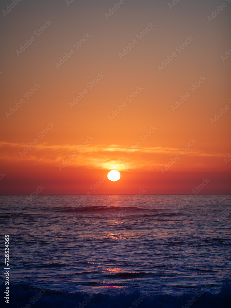 A bright sunset on the vibrant orange sky over the Atlantic Ocean. Vertical photo with empty space for text