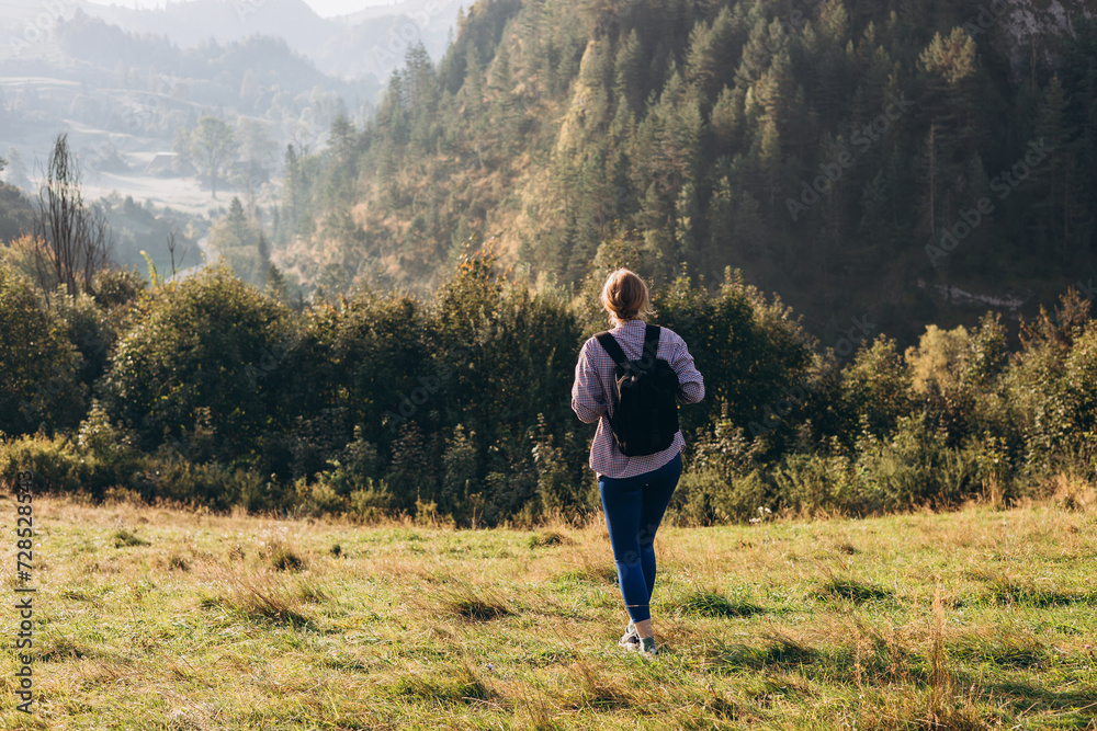 30s Girl with backpack on mountain peak with green grass looking at beautiful mountain valley in fog at sunset in summer. Landscape with sporty young woman, rear view. Full body 30s Girl with backpack on mountain peak with green grass looking at beautiful mountain valley in fog at sunset in summer. Landscape with sporty young woman, rear view. Full body
