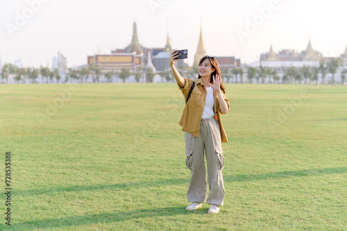 Traveler asian woman in her 30s take a livestream on smartphone while explores Wat Phra Kaew emerald Buddha. Share the wonders of Thai heritage through her journey.