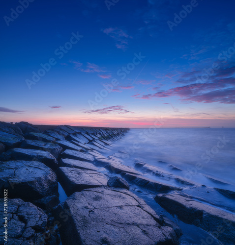 A seascape during sunset. The stone causeway during sunset. Sharp rocks. Bright sky during sunset. Long exposure. Photo for wallpaper.