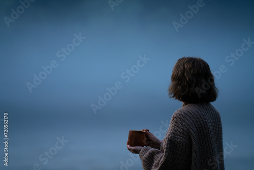 A woman in a sweater on the bank of a foggy river in the evening.. © scharfsinn86