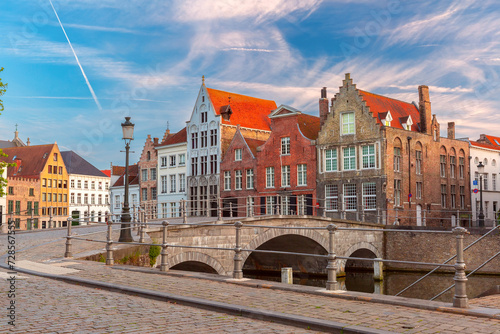 Scenic city view of Bruges canal, medieval houses and sunny bridge at sunset, golden hour, Belgium
