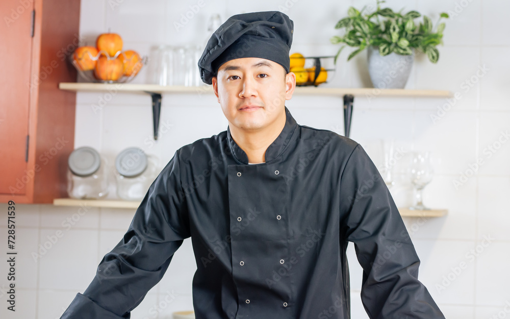 Portrait handsome professional Japanese male chef wearing black uniform, hat, cooking, smiling with confidence, happiness, standing in kitchen. Restaurant, Hotel Concept. Portrait handsome professional Japanese male chef wearing black uniform, hat, cooking, smiling with confidence, happiness, standing in kitchen. Restaurant, Hotel Concept.