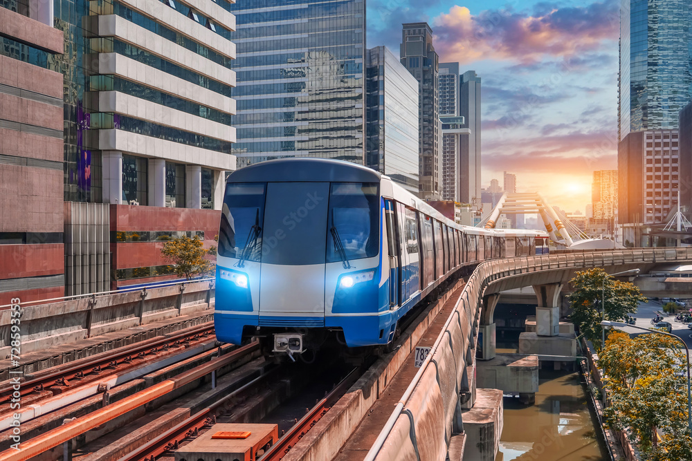 Naklejka premium Electric train bright light railway carriage rushes turn travels along route in sunset sky railway road viaduct among the modern city of buildings, skyscrapers metropolis
