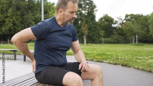 A handsome middle-aged Caucasian man has a backache on a bench in a park