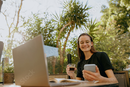 Ypung businesswoman reading message on phone and work on laptop outside of office