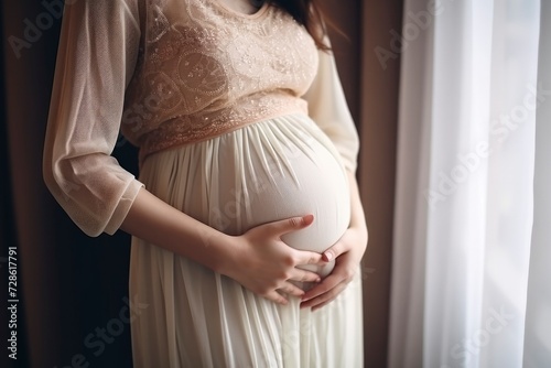 A young pregnant woman in delicate dress holds her hands on her stomach close-up. The concept of happy expectation of a child, motherhood, pregnancy. 