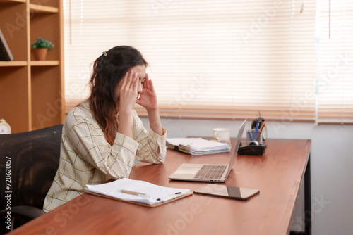 фотографія Engulfed in work stress,  Asian businesswoman covers face, gesture of frustration in a quiet office
