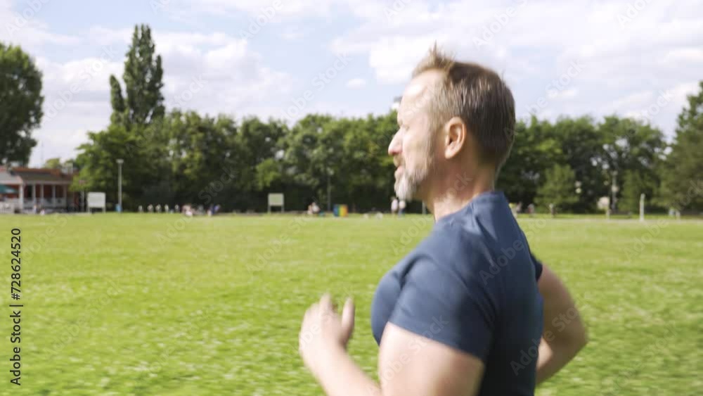 A handsome middle-aged Caucasian man jogs in a park on a sunny day - side closeup A handsome middle-aged Caucasian man jogs in a park on a sunny day - side closeup