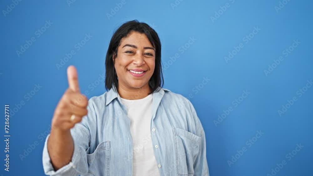 Middle-aged hispanic woman giving thumbs up against a blue isolated background, exuding confidence and approval. Middle-aged hispanic woman giving thumbs up against a blue isolated background, exuding confidence and approval.