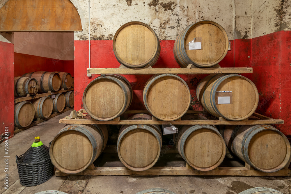 Wooden barriques for wine aging are arranged on three levels in a Tuscan cellar