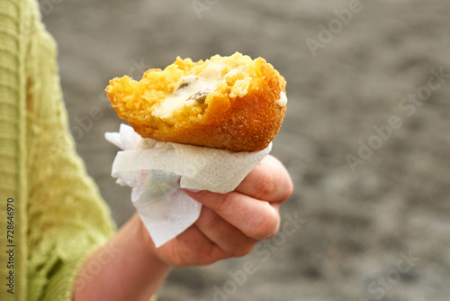 Woman's hand at seaside holding hot palatable arancino (deep fried rice balls with meat). Typical Sicilian street food. Close up.
