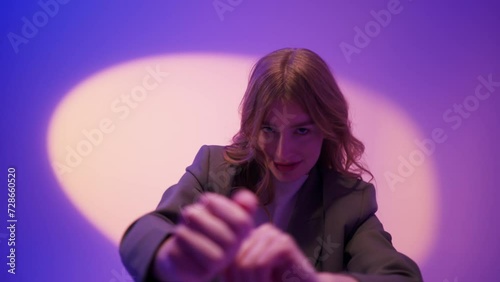 Young woman 20s in formal jacket dancing and posing isolated on neon purple violet background studio