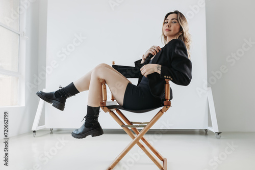 portrait of a young blonde beautiful business woman sitting on a directors chair in black skirt, jacket and boots