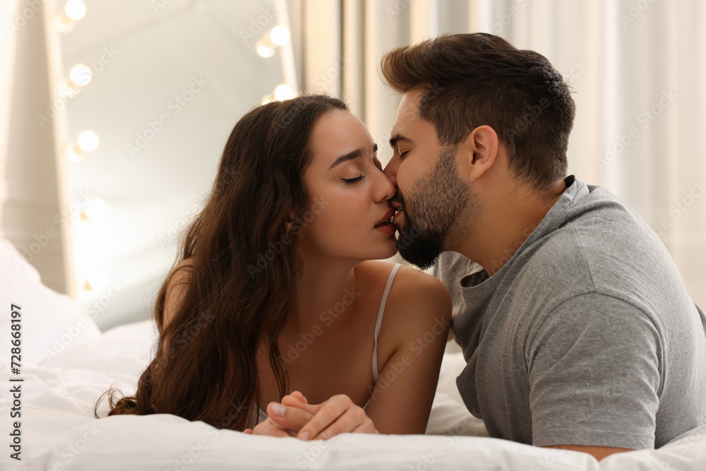 Passionate young couple kissing on bed indoors Passionate young couple kissing on bed indoors