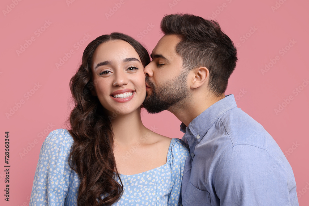 Man kissing his smiling girlfriend on pink background Man kissing his smiling girlfriend on pink background