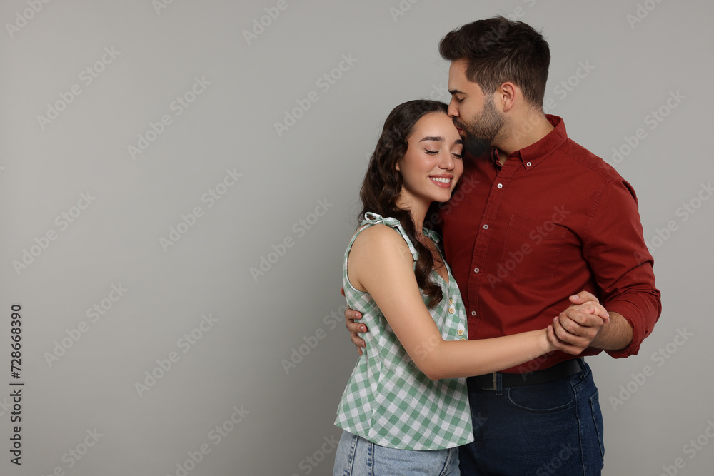 Man kissing his smiling girlfriend on grey background. Space for text Man kissing his smiling girlfriend on grey background. Space for text
