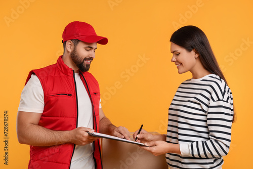 Happy young woman signing order receipt on orange background. Courier delivery
