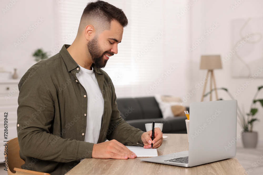 Young man writing in notebook at wooden table indoors Young man writing in notebook at wooden table indoors