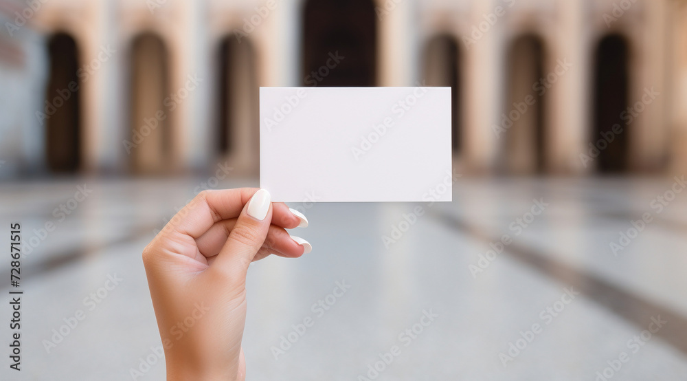 Close-up of a hand presenting a blank business card with an urban backdrop. Close-up of a hand presenting a blank business card with an urban backdrop.