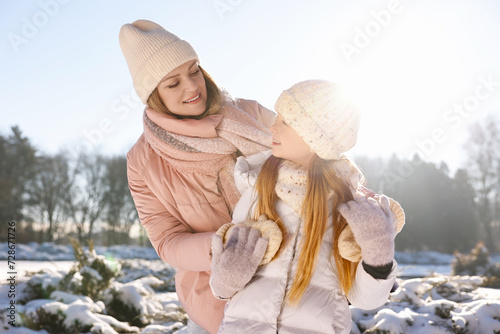 Family portrait of happy mother and her daughter in sunny snowy park