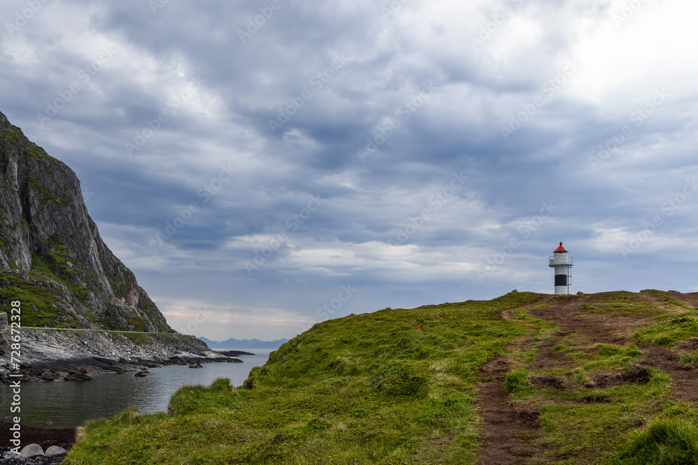 A path leads to the Borhella lighthouse, a solitary figure against a dramatic sky, on Norway's rugged coastal landscape