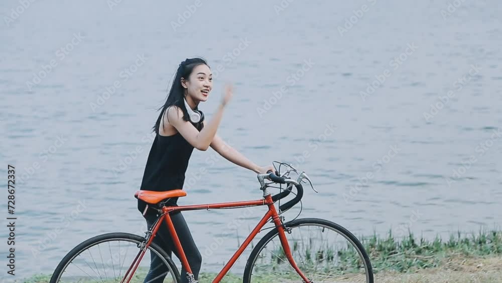 Happy young Asian woman while riding a bicycle in a city park. She smiled using the bicycle of transportation. Environmentally friendly concept.