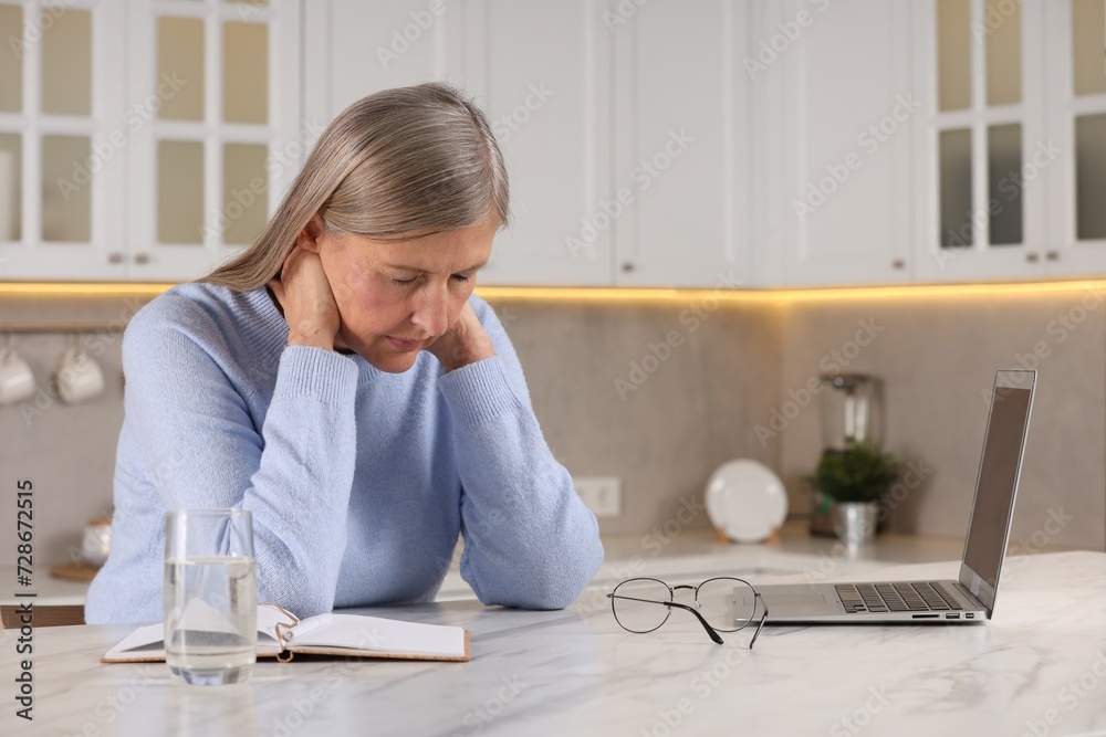 Menopause. Woman suffering from pain in neck at table in kitchen, space for text Menopause. Woman suffering from pain in neck at table in kitchen, space for text