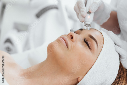 A professional esthetician uses the RF Lifting procedure to rejuvenate and tighten the skin of the client's face. Vacuum Facial Massage for Woman's Skin Care photo