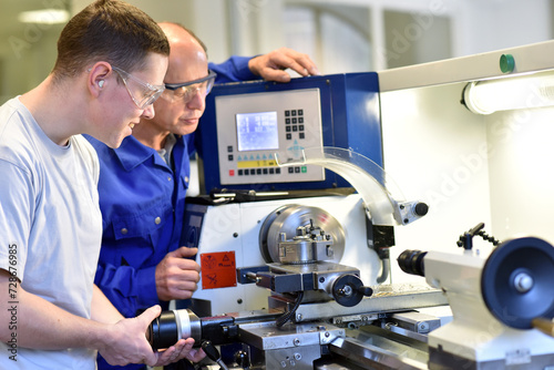 young apprentices in technical vocational training are taught by older trainers on a cnc lathes machine photo
