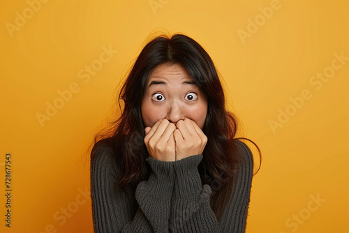 Nervous, Asian woman and biting nails in studio with oops reaction to gossip on yellow background. Mistake, sorry and female overwhelmed by fake news, drama or secret with regret, shame or awkward photo