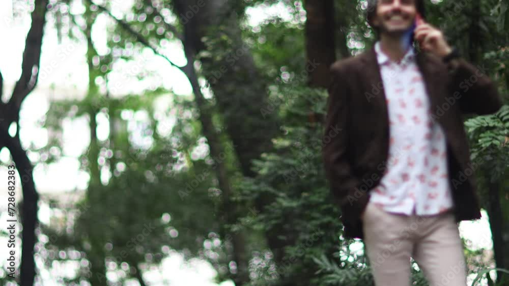 View of a young man with smartphone at daytime in a green park in the city. 
High quality video