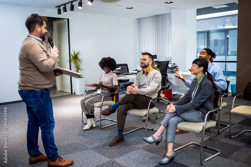 Fototapeta premium Bussines man lecturing his multiethnic colleagues. Having a speach while holding a microphone.