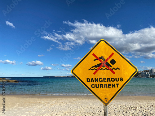 Warning sign on the beach indicating a dangerous current. Yellow panel to highlight a potential danger in the water.
