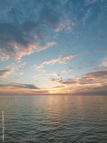Tranquil Evening Seascape, Summer Sunset Casting Warm Glow Over Calm Waters with Clouds, Serene Beauty of Dusk