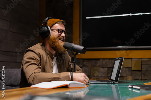 Smiling and gesturing radio host with headphones reading news into studio microphone photo