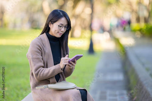 Woman use of mobile phone and sit on bench at park
