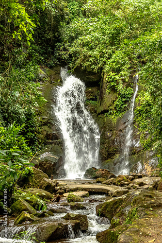 Waterfall running between rocks at the foot of the mountain  Waterfall running between the rocks at the foot of the mountain  creating a winding and refreshing path. The tumultuous water splashes in a