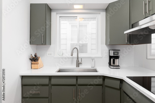 A kitchen detail with green cabinets, white countertop, and a subway tile backsplash.