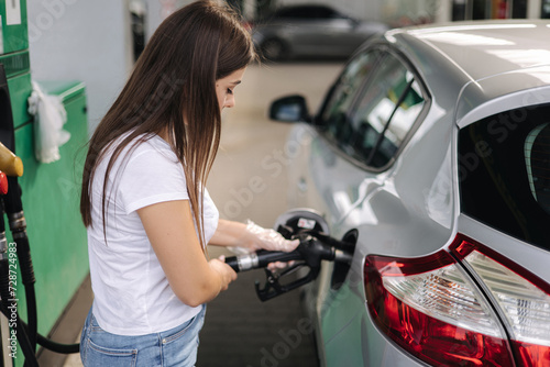 Attractive young woman refueling car at gas station. Female filling diesel at gasoline fuel in car using a fuel nozzle. Petrol concept. Side view