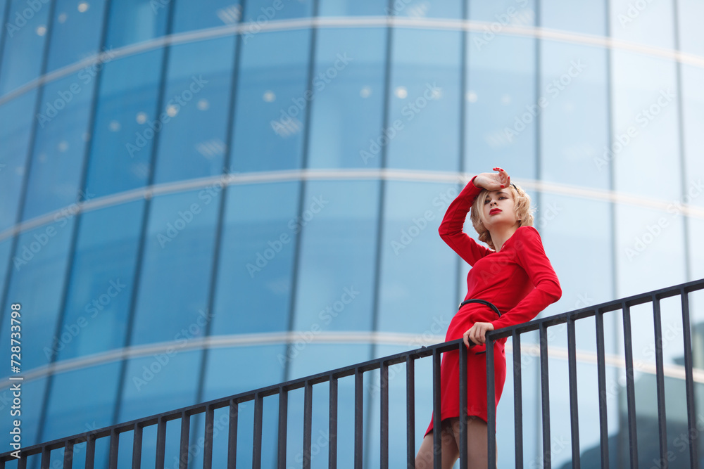 Woman in red on a background of glass walls reflecting blue sky