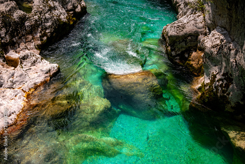 Cascade and current of Soča (Emerald River) in Slovenia, pristine wild alpine river with crystal clear water and intense turquoise green color. Natural reserve and national park on a sunny summer day.