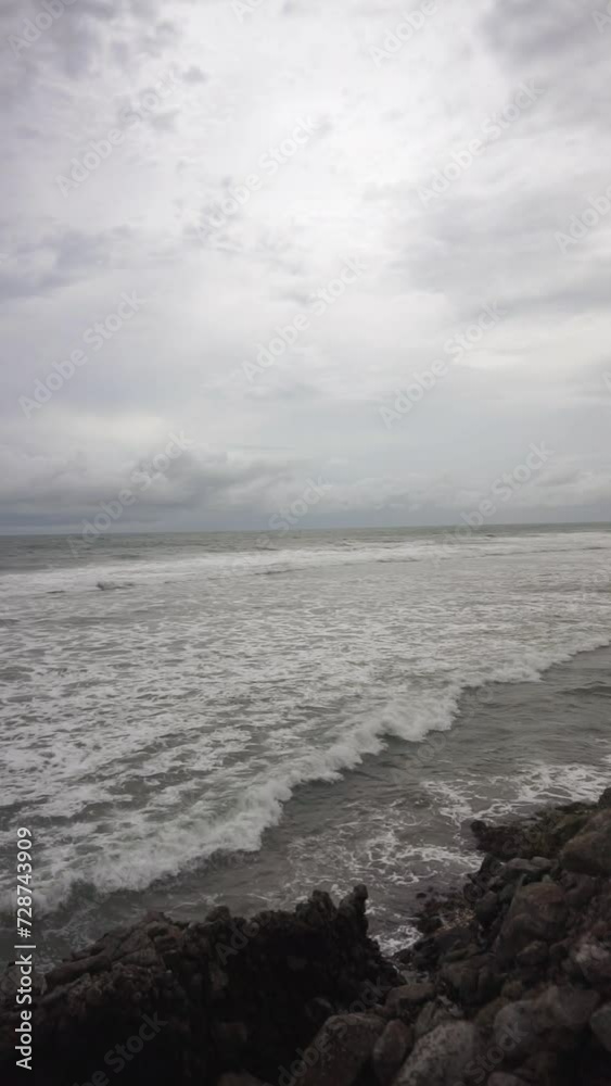 Beautiful vertical video of beachside views, natural panoramas, sea water accompanied by crashing waves and coral rocks with cloudy skies in the afternoon, on Karang Paranje beach, Garut