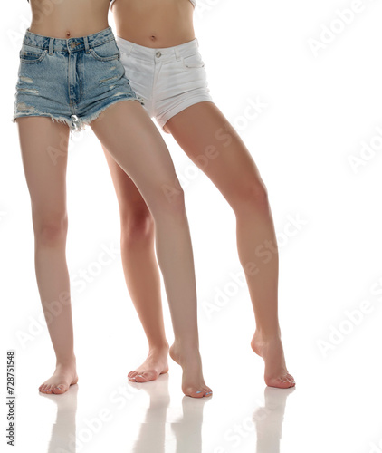 Two pairs od a beautiful well-groomed women's legs close-up in shorts on a white isolated studio background, The concept of epilation of foot skin care.